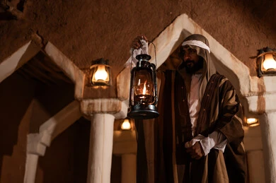 رجل سعودي يحمل فانوساً في بيت طيني تراثي