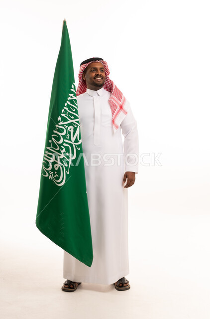 رجل سعودي بالزي التقليدي مع علم المملكة العربية السعودية