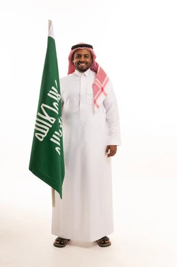 رجل سعودي بالزي التقليدي يحمل العلم الوطني