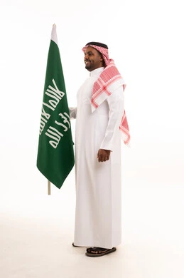 رجل سعودي يرتدي الزي التقليدي يحمل العلم