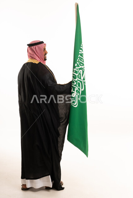 رجل سعودي بالزي التقليدي مع علم المملكة العربية السعودية