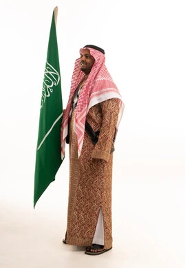رجل سعودي بالزي التقليدي يحمل علم المملكة العربية السعودية