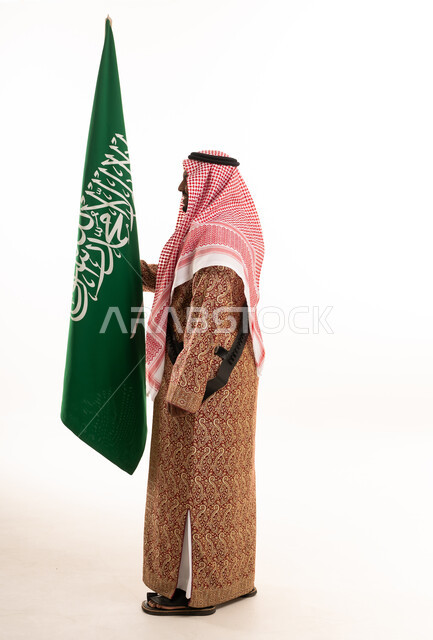 رجل سعودي يرتدي الزي التقليدي يحمل علم المملكة