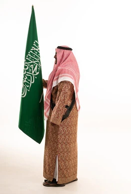 رجل سعودي يرتدي الزي التقليدي يحمل علم المملكة