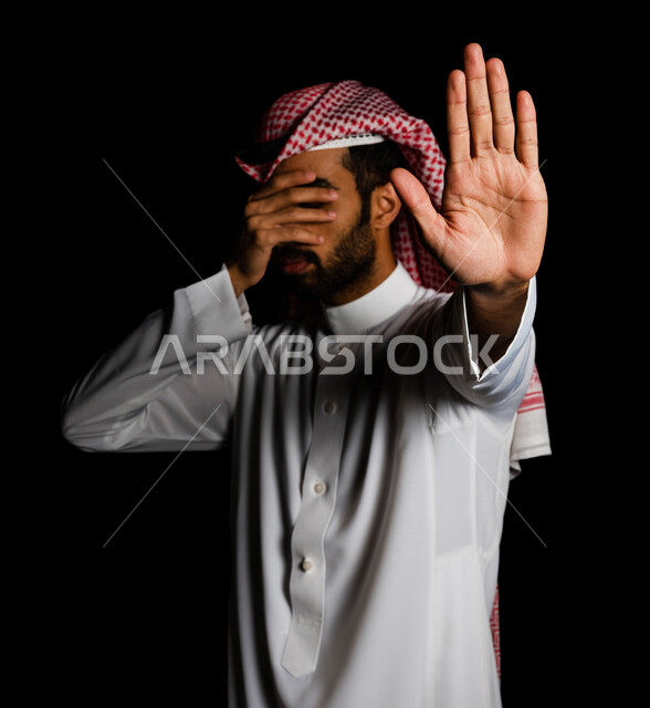 رجل عربي سعودي خليجي يرتدي الزي السعودي, إيماءات يدين تدل على الأمر بالتوقف عن فعل شيء ما, النهي عنه, الشعور بالإنزعاج, الرفض والإمتناع, خلفيه سوداء