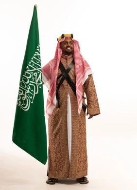 رجل سعودي يمسك علم السعودية بزي العرضة الشعبية التقليدي
