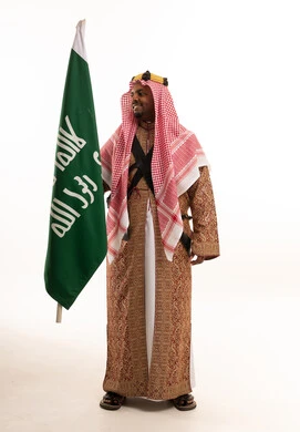 رجل سعودي يحمل العلم الوطني بالزي التقليدي الرسمي