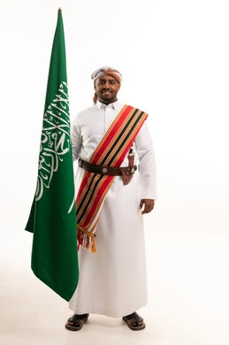 رجل سعودي بالزي التراثي التقليدي يحمل العلم الوطني
