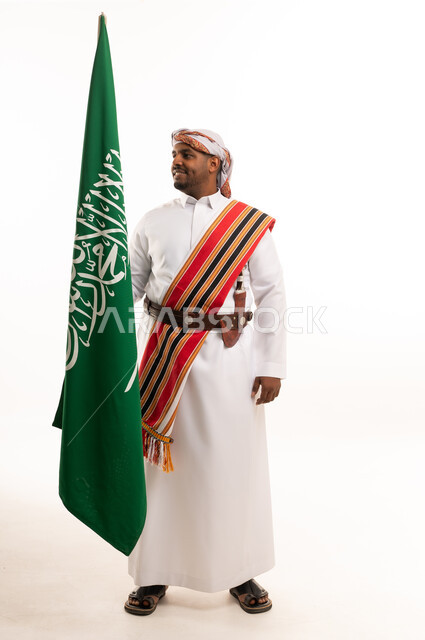 رجل سعودي يحمل العلم الوطني بالزي الشعبي التقليدي