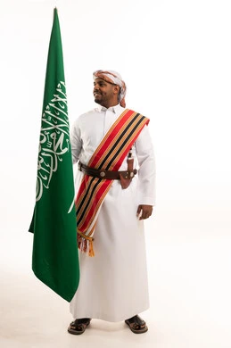 رجل سعودي يحمل العلم الوطني بالزي الشعبي التقليدي