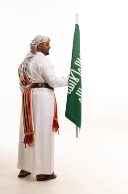 رجل سعودي يرتدي الزي الوطني التقليدي يحمل علم السعودية