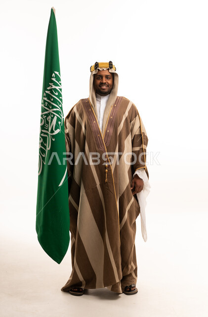 رجل سعودي يحمل العلم الوطني السعودي بالبشت التقليدي