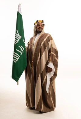 رجل سعودي يحمل العلم بالبشت التقليدي المقلم