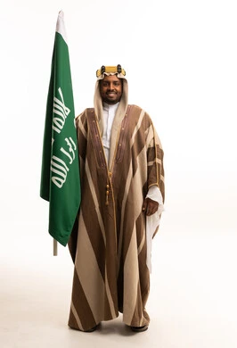 رجل سعودي بالبشت التقليدي يحمل علم المملكة العربية السعودية