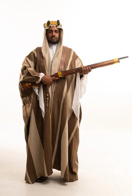 رجل سعودي يرتدي البشت التقليدي ويحمل بندقية تراثية قديمة