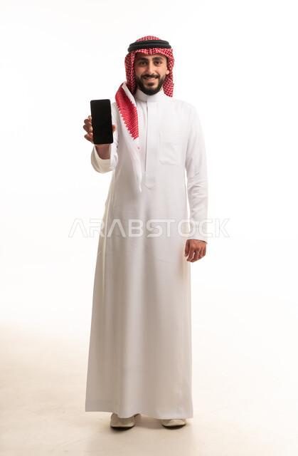 رجل سعودي بالزي التقليدي يحمل هاتفاً ذكياً خلفية بيضاء