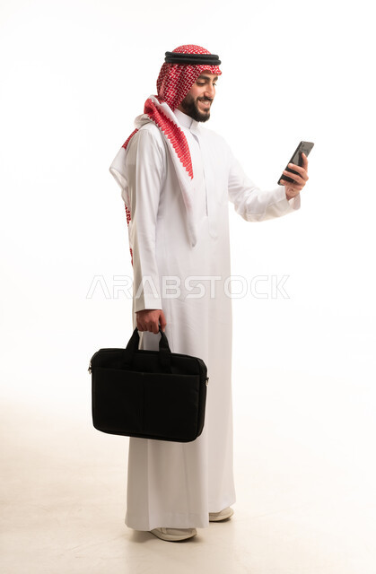 رجل سعودي يحمل حقيبة لابتوب وهاتف ذكي في استوديو