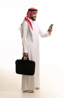 رجل سعودي يحمل حقيبة لابتوب وهاتف ذكي في استوديو
