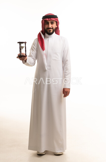 رجل سعودي بالزي التقليدي يحمل ساعة رملية