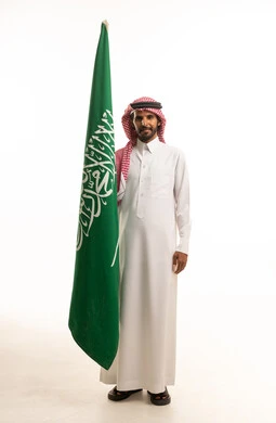 رجل سعودي يحمل علم المملكة العربية السعودية بالزي التقليدي