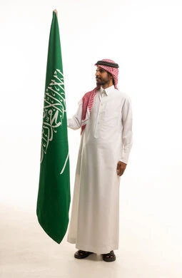 رجل سعودي بالزي التقليدي يحمل علم المملكة العربية السعودية