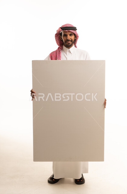 رجل سعودي يحمل لوحة بيضاء فارغة في استوديو