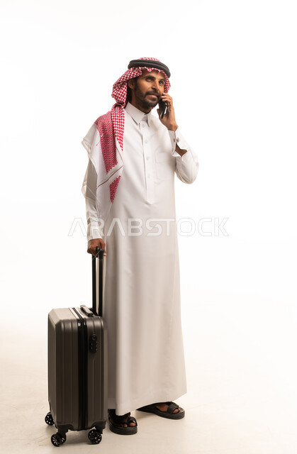 رجل سعودي بالزي التقليدي مع حقيبة سفر وهاتف محمول