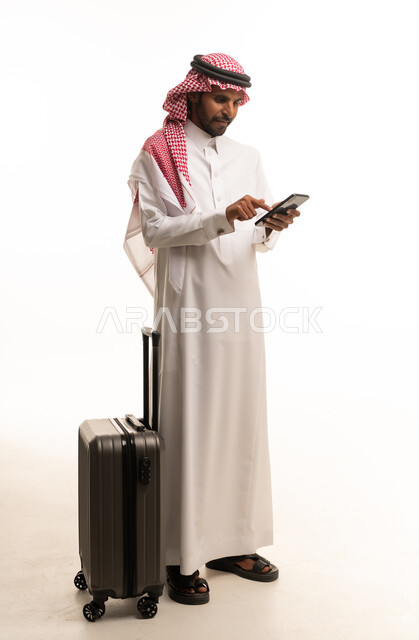 رجل سعودي بالزي التقليدي مع حقيبة سفر وهاتف ذكي