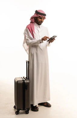 رجل سعودي بالزي التقليدي مع حقيبة سفر وهاتف ذكي