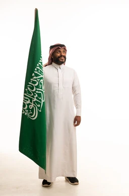رجل سعودي يحمل العلم الوطني على خلفية بيضاء
