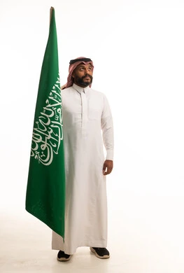 رجل سعودي يحمل العلم الوطني على خلفية بيضاء