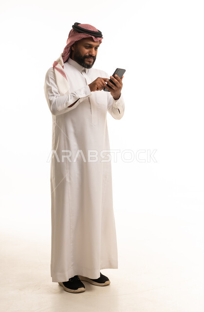 رجل سعودي بالثوب التقليدي يستخدم الهاتف الذكي