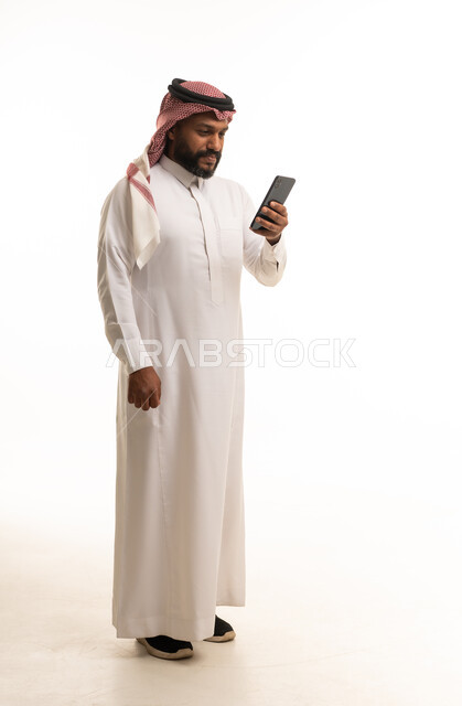 رجل سعودي بالزي التقليدي يستخدم هاتف ذكي بخلفية بيضاء
