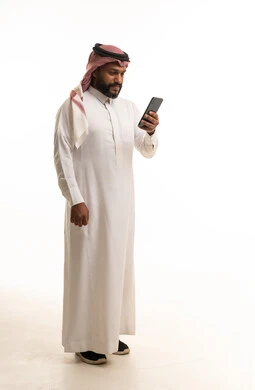 رجل سعودي بالزي التقليدي يستخدم هاتف ذكي بخلفية بيضاء