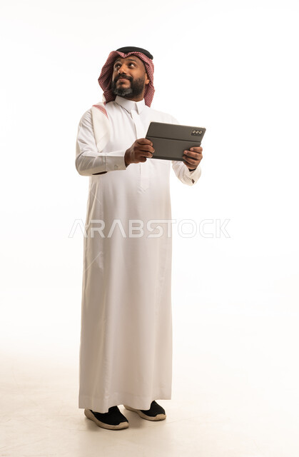رجل سعودي يحمل جهاز لوحي أمام خلفية استوديو بيضاء