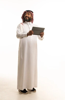 رجل سعودي يحمل جهاز لوحي أمام خلفية استوديو بيضاء