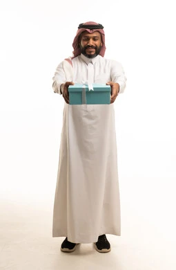 رجل سعودي يحمل صندوق هدايا أزرق على خلفية بيضاء