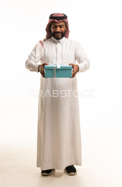 رجل سعودي يحمل صندوق هدايا أزرق بخلفية بيضاء