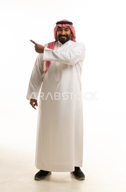 رجل سعودي يرتدي الثوب التقليدي يشير لجانب بخلفية بيضاء
