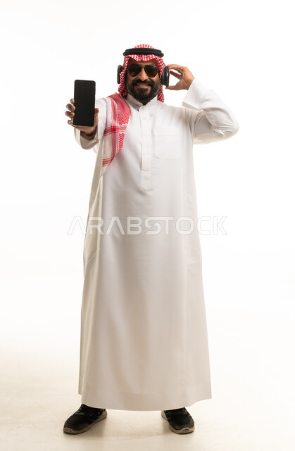 رجل سعودي يرتدي سماعات وهاتف ذكي خلفية بيضاء
