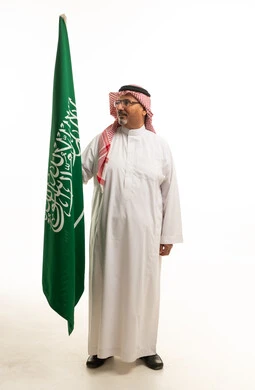 رجل سعودي بالزي التقليدي يمسك علم السعودية