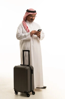 رجل سعودي يحمل حقيبة سفر ويستخدم الهاتف الذكي