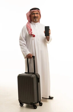 رجل سعودي مع حقيبة سفر يحمل هاتفاً ذكياً في استوديو