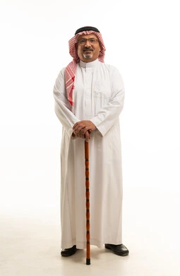 رجل سعودي مسن يحمل عصا مشي بخلفية بيضاء
