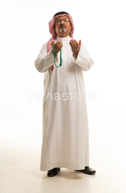 رجل سعودي بالزي التقليدي يدعو وبيده سبحة خلفية بيضاء