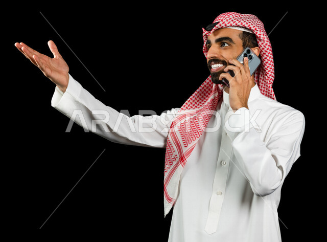 رجل عربي خليجي سعودي يجري اتصال من خلال الهاتف المحمول، اجراء مكالمة هاتفية، إتصال و تعارف، دردشه ومحادثات, علاقات إجتماعية، ايماءات وجه تدل على السعاده، خلفية سوداء