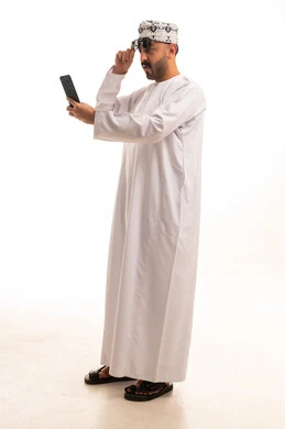 Omani Man in White Dishdasha Using Smartphone