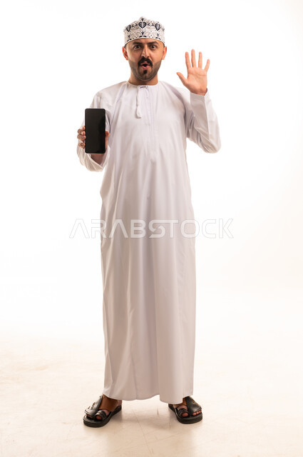 رجل عماني يحمل هاتف ذكي بتعبير مندهش