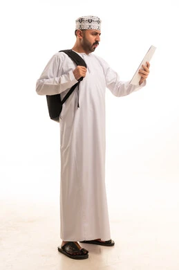 رجل عُماني باللباس التقليدي يحمل جهازاً لوحياً وحقيبة