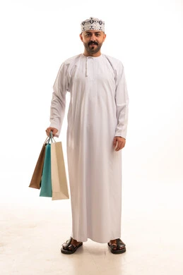 رجل عُماني يرتدي الزي التقليدي يحمل حقائب تسوق ملونة